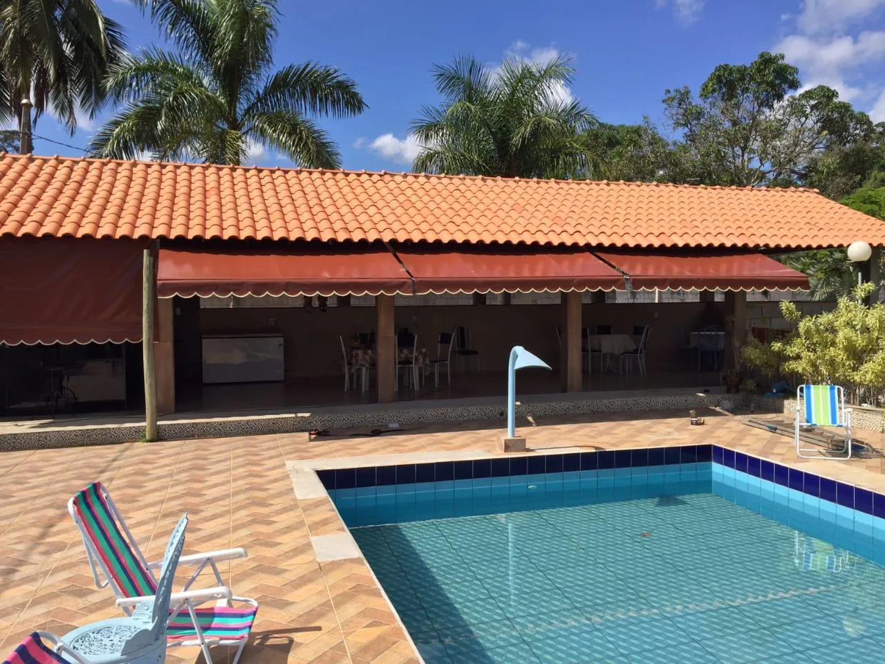 Toldo retrátil com braços em lona laranja sombreando área de piscina